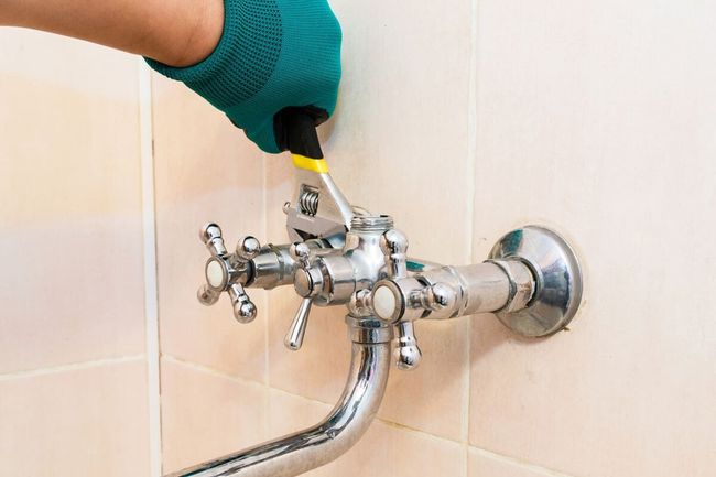 Una persona está arreglando un grifo del baño con una llave inglesa.