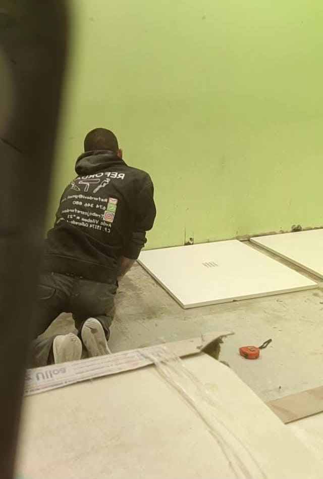 Un hombre está arrodillado en el suelo mientras instala baldosas.