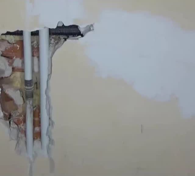 Una tubería sale de un agujero en una pared.
