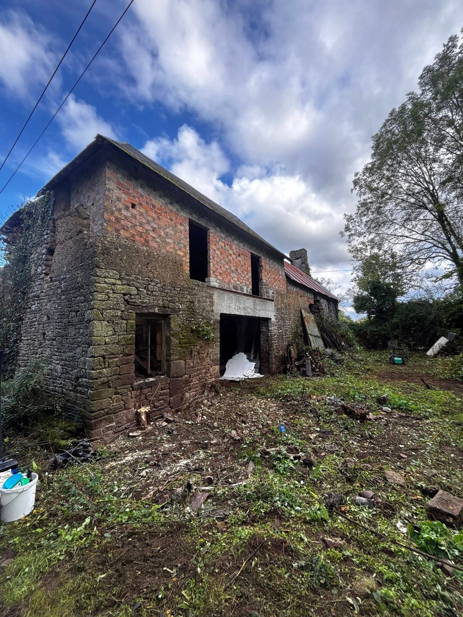 Maison délabrée en pierre et en brique; cour envahie par la végétation.