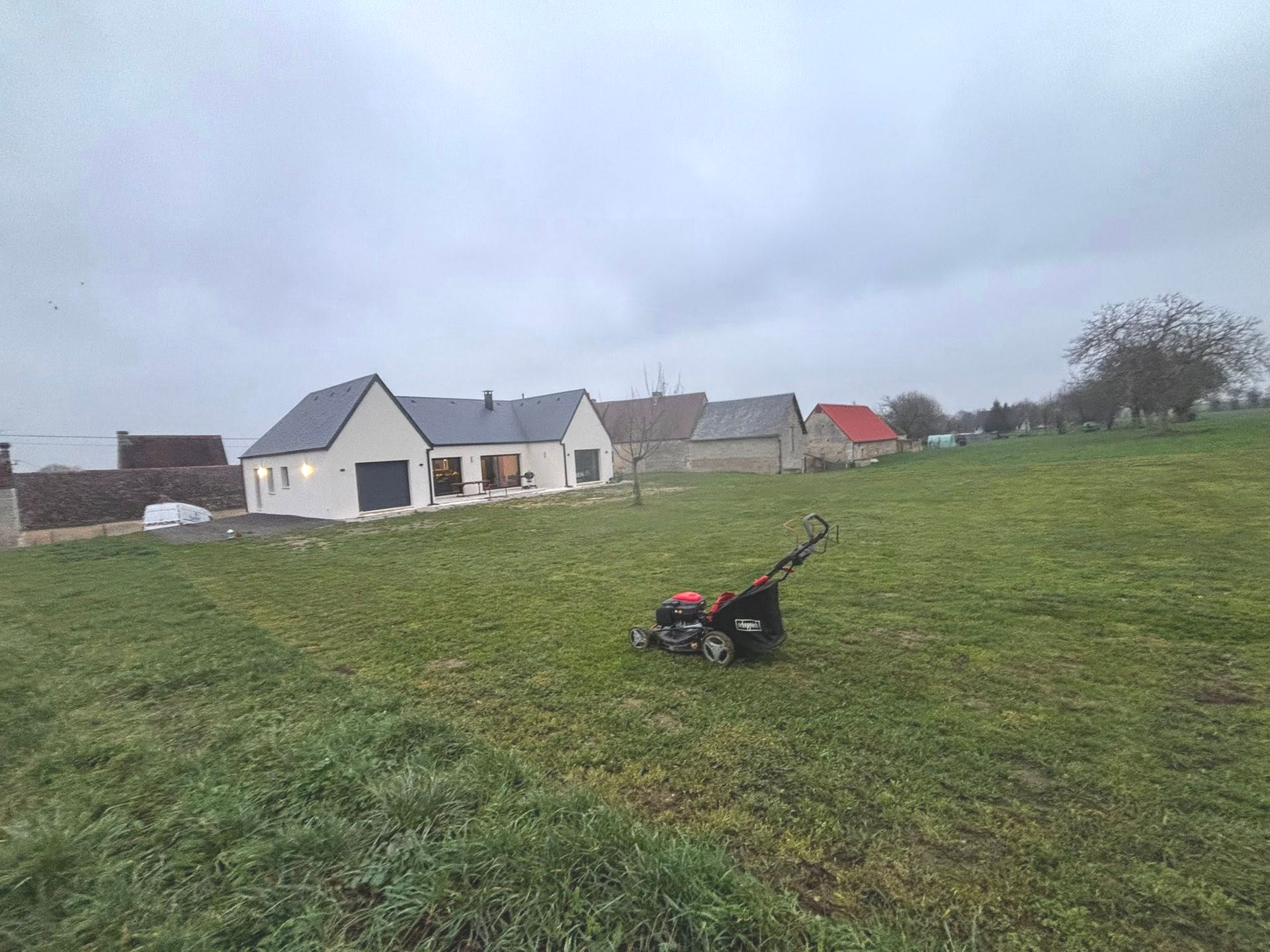 Tondeuse à gazon sur une colline herbeuse devant une maison.