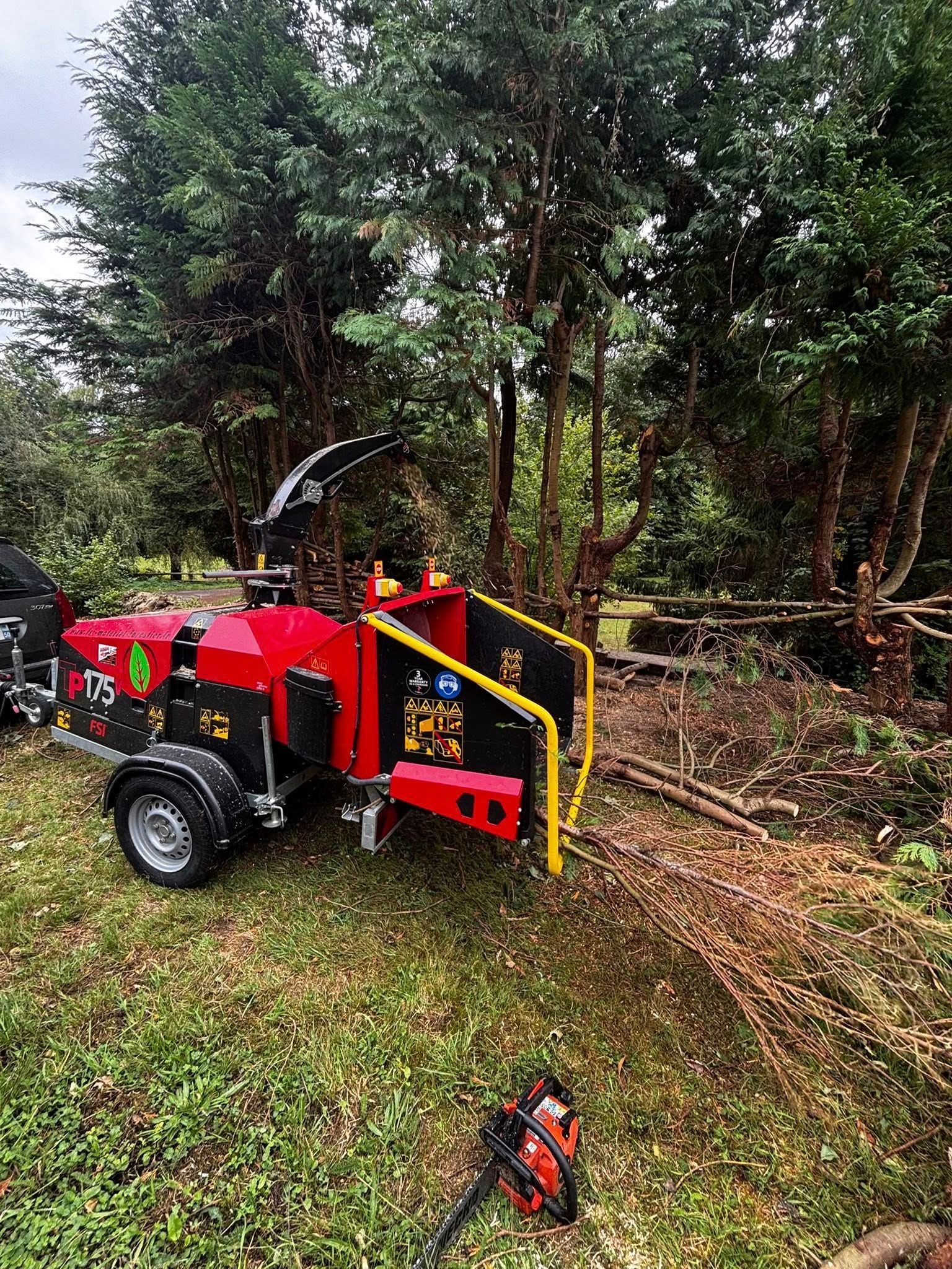 Broyeur de bois rouge traitant des branches dans une clairière herbeuse avec des arbres.