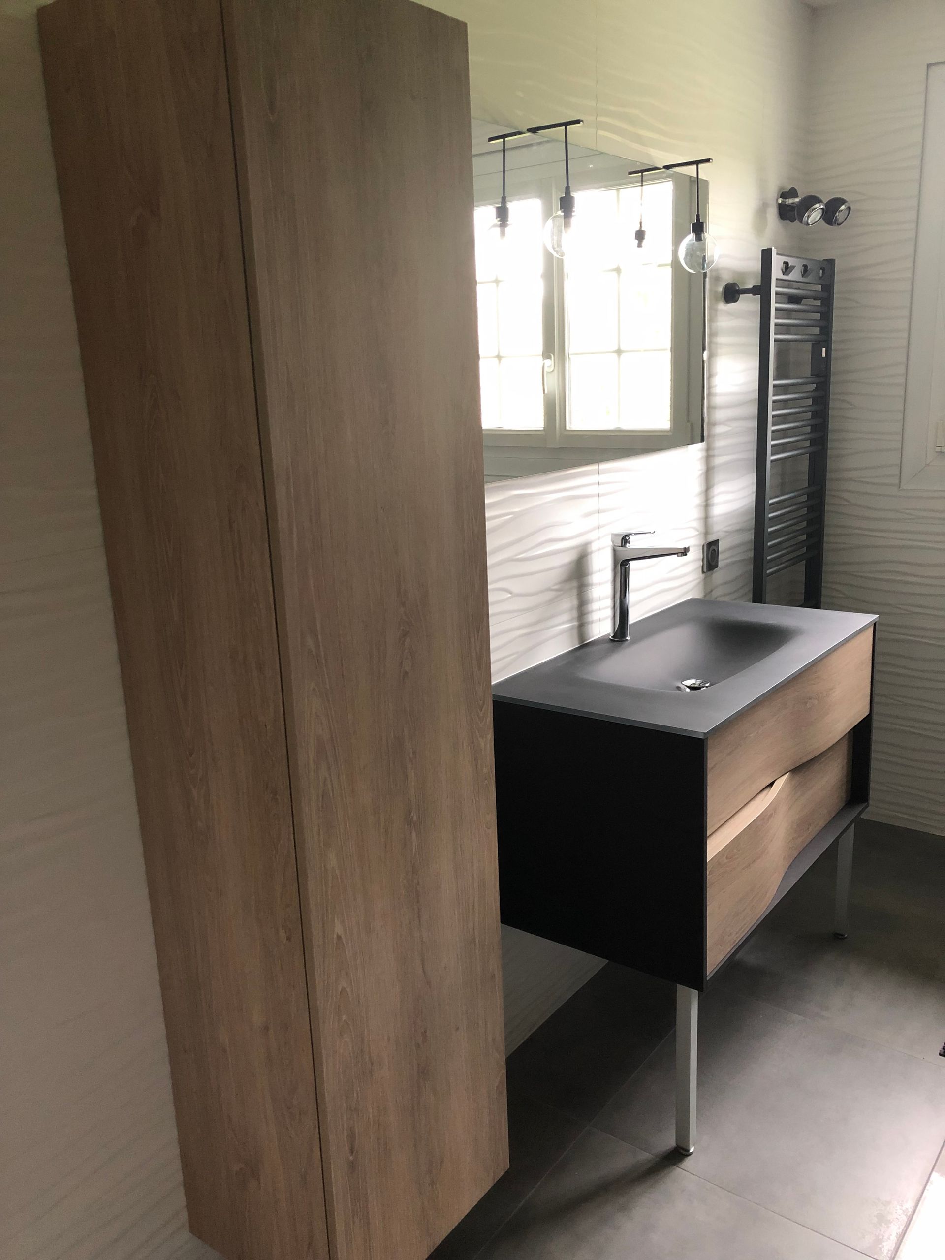 Petite salle de bains avec meuble-lavabo en bois, lavabo noir, miroir et porte-serviettes.