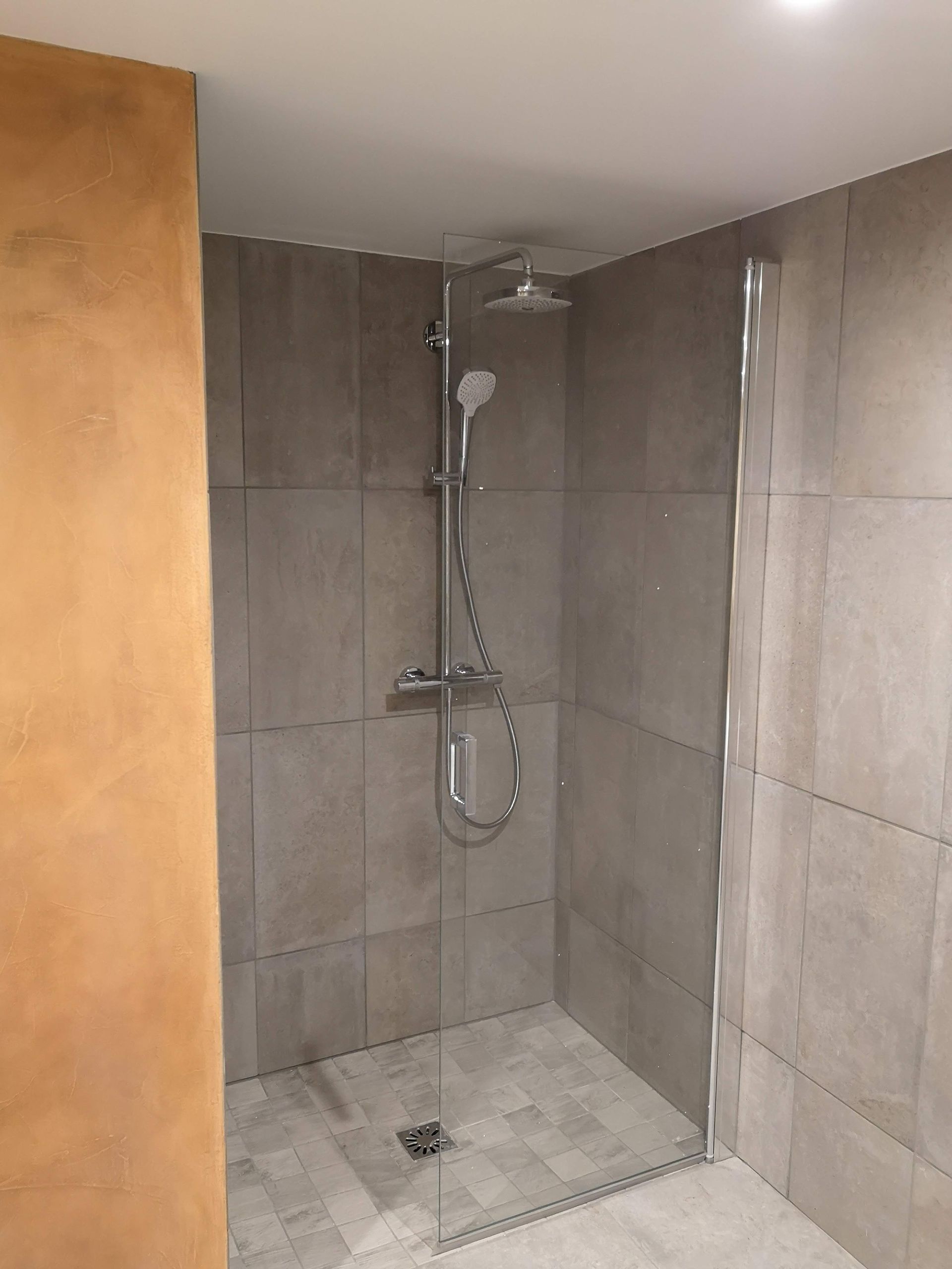 Douche à l'italienne, visible à travers une porte en bois entrouverte.