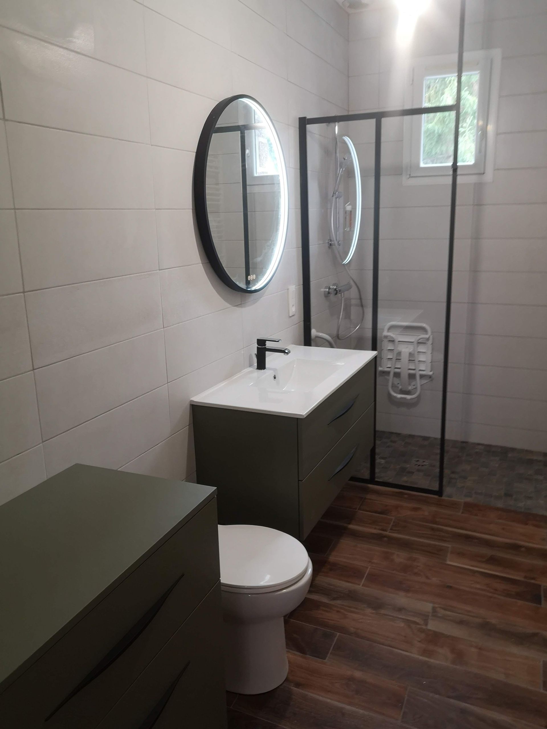 Salle de bains moderne avec meuble-lavabo foncé, miroir ovale, toilettes et cabine de douche.