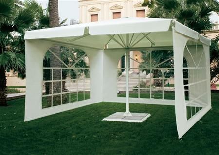 Una tienda de campaña blanca con una sombrilla en medio de un exuberante campo verde.