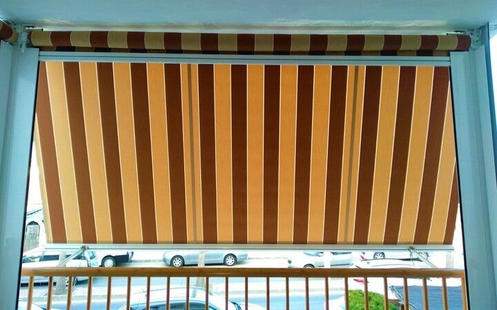 Un toldo de rayas marrones y amarillas cuelga sobre un balcón.