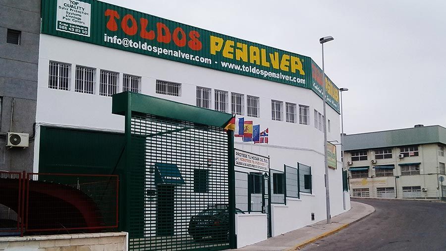 Un edificio blanco con un cartel verde que dice toldos peralver