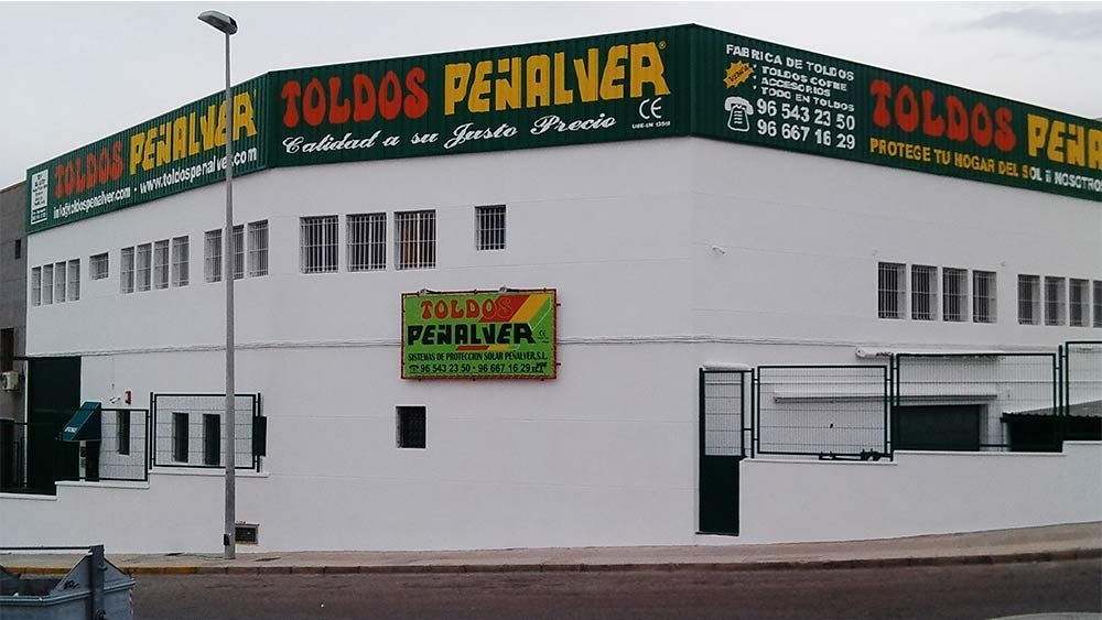 Un edificio blanco con un cartel verde que dice toldos penalver