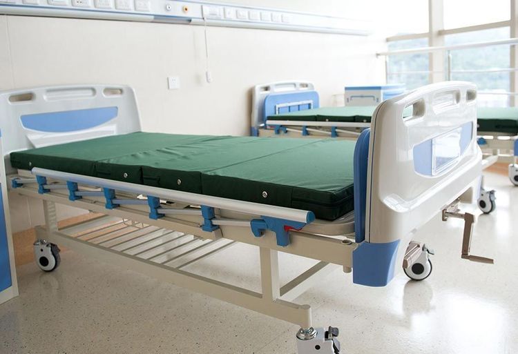 Una fila de camas de hospital con colchones verdes en una habitación de hospital.