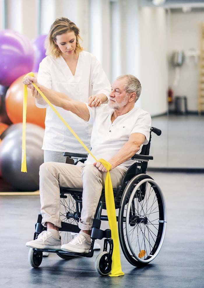 Una mujer está ayudando a un anciano en silla de ruedas con una banda de resistencia.