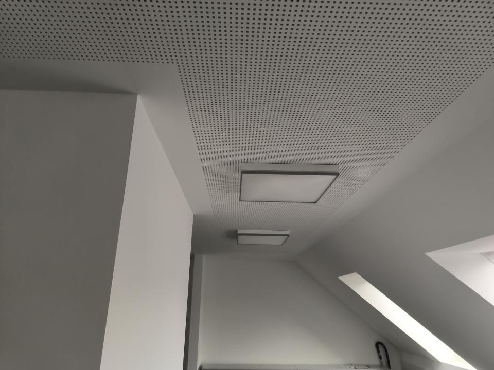 Weiße Zimmerdecke mit Lochblech und zwei rechteckigen Deckenleuchten.