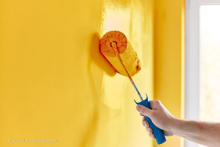 Person, die mit einer Farbrolle eine gelbe Wand streicht, Hand im Vordergrund.