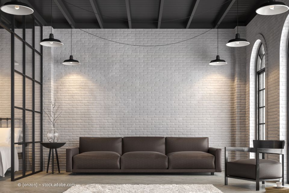 Modernes Wohnzimmer mit braunem Sofa vor einer weißen Ziegelwand, drei Pendelleuchten und einer Glaswand mit schwarzem Rahmen.