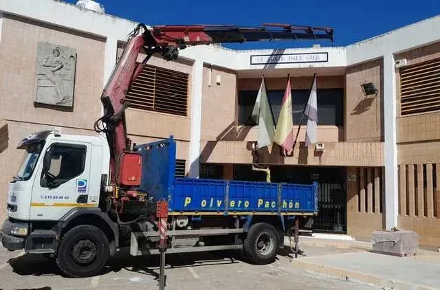Un camión con una grúa en la parte trasera está estacionado frente a un edificio.