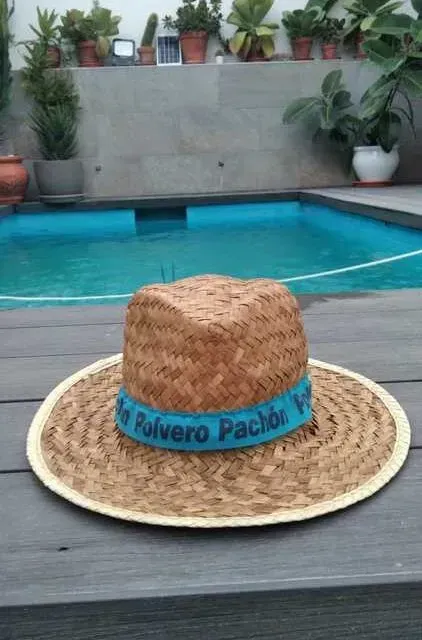 Un sombrero de paja reposa sobre una terraza de madera frente a una piscina.