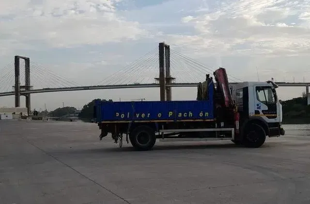 Un camión azul está estacionado frente a un puente.