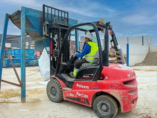 Un hombre conduce una carretilla elevadora roja en un sitio de construcción.