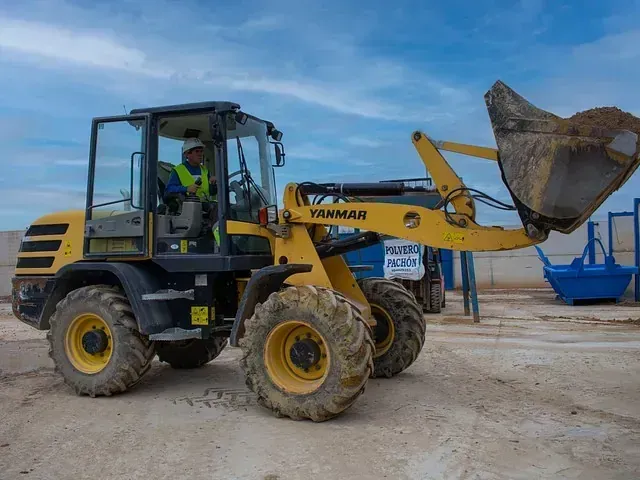 Un hombre conduce una cargadora de ruedas amarilla y negra por un camino de tierra.