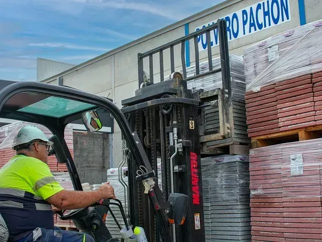 Un hombre conduce una carretilla elevadora delante de un edificio.