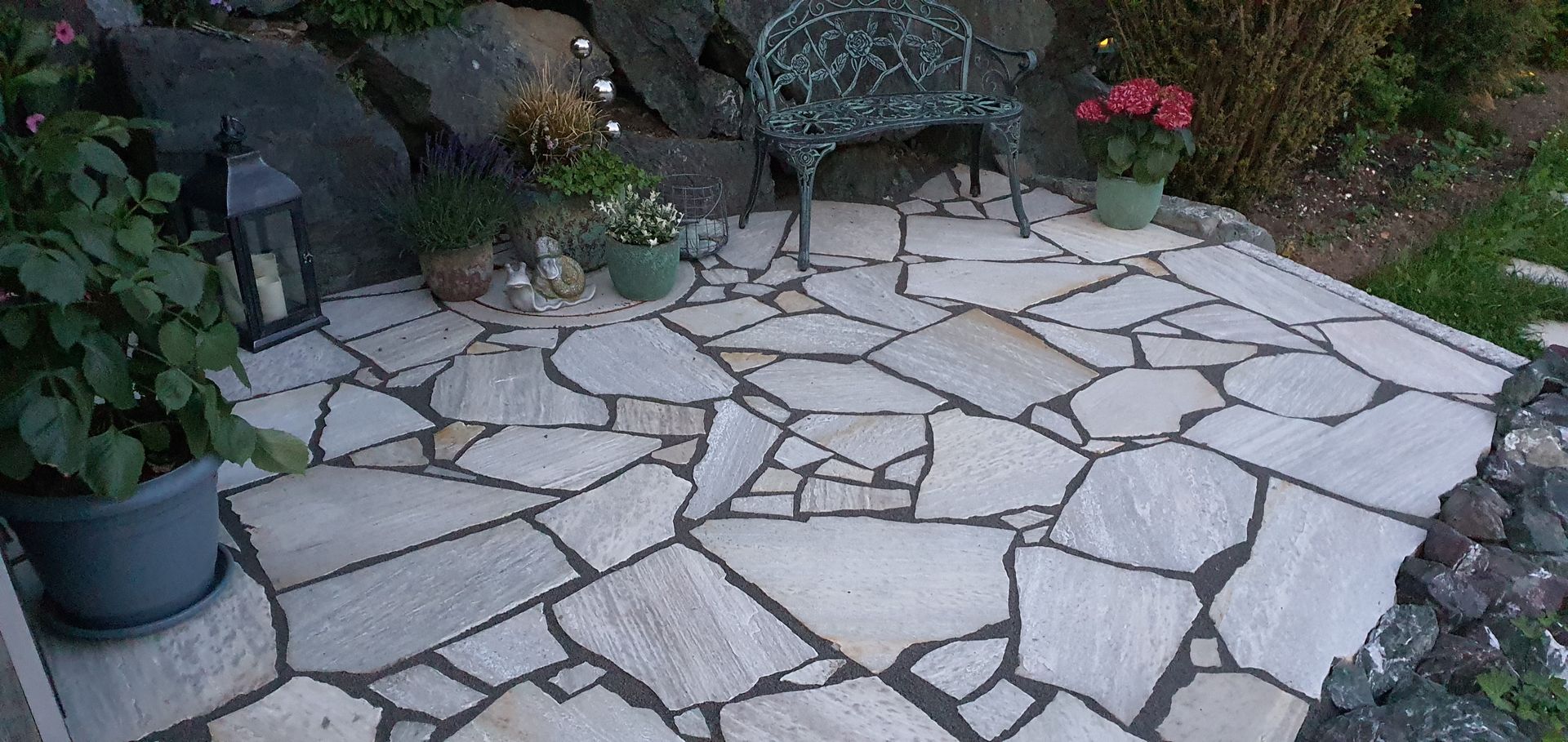 Moderner, landschaftlich gestalteter Gartenweg mit Steinplatten, weißem Kies und geschnittenen grünen Sträuchern in der Abenddämmerung