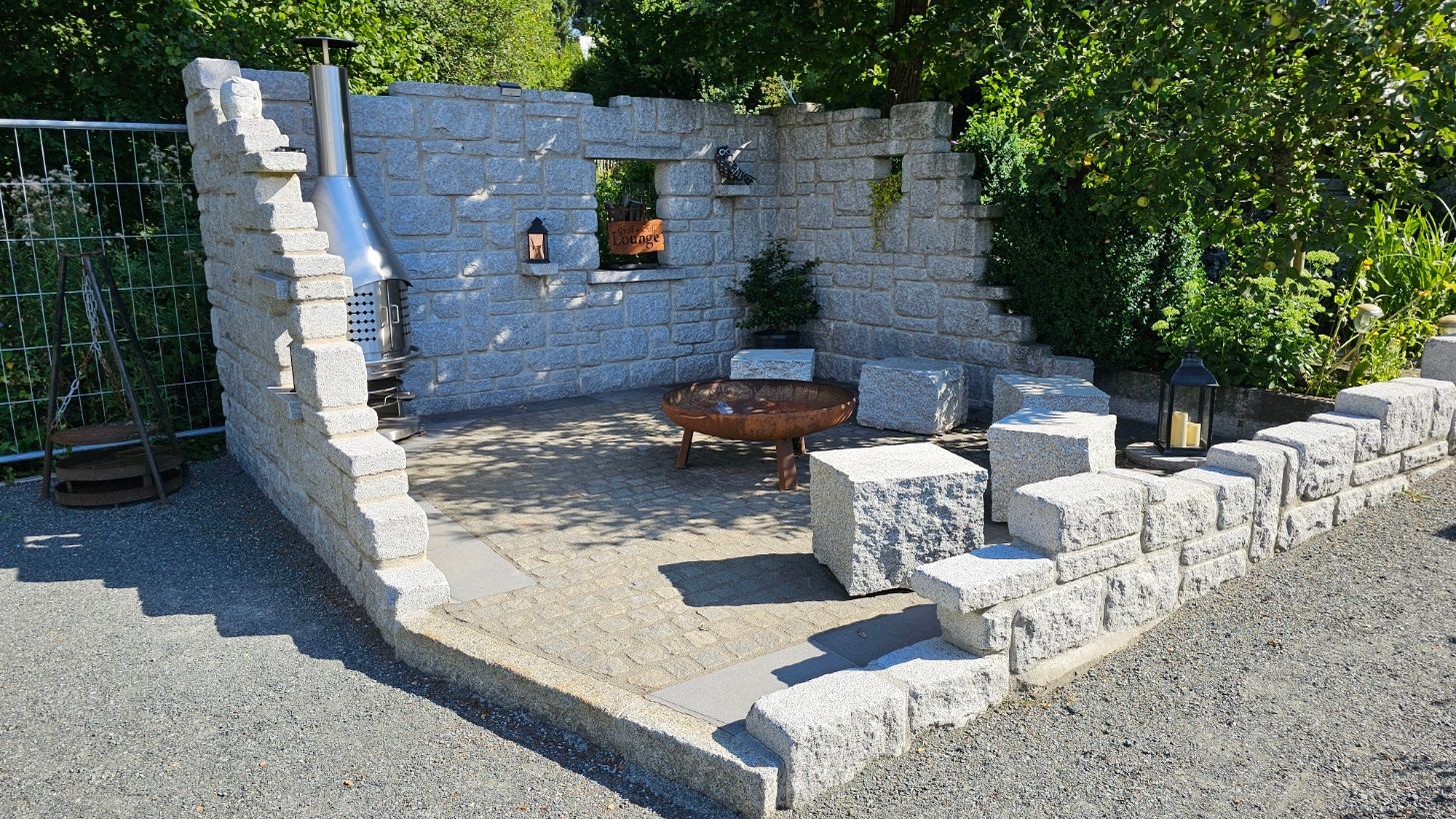 Überdachte Terrasse mit grauem Ecksofa, Korbtischen und Blick in den grünen Garten