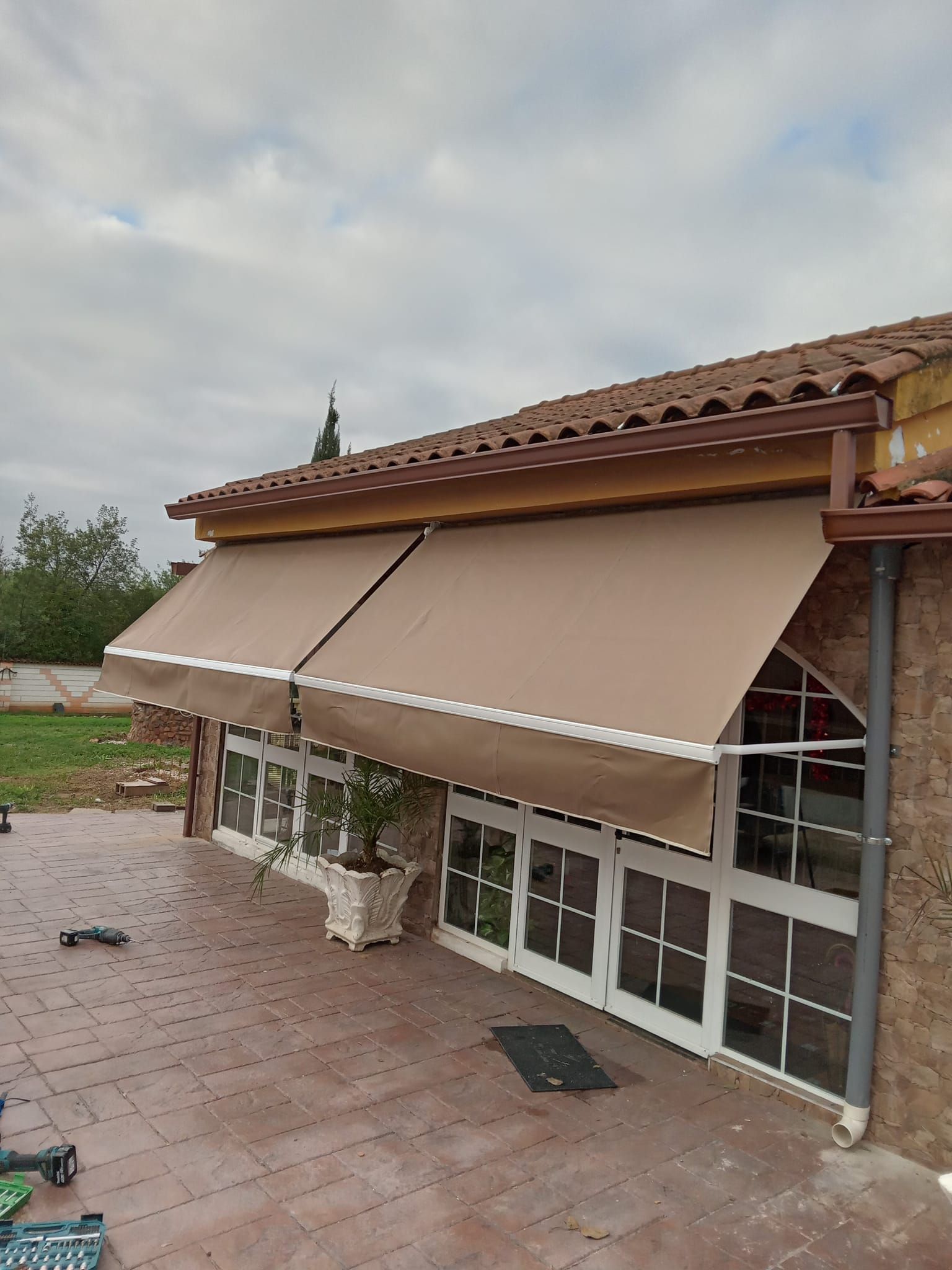 Toldos beige sobre las ventanas de una casa de ladrillo. Cielo nublado.