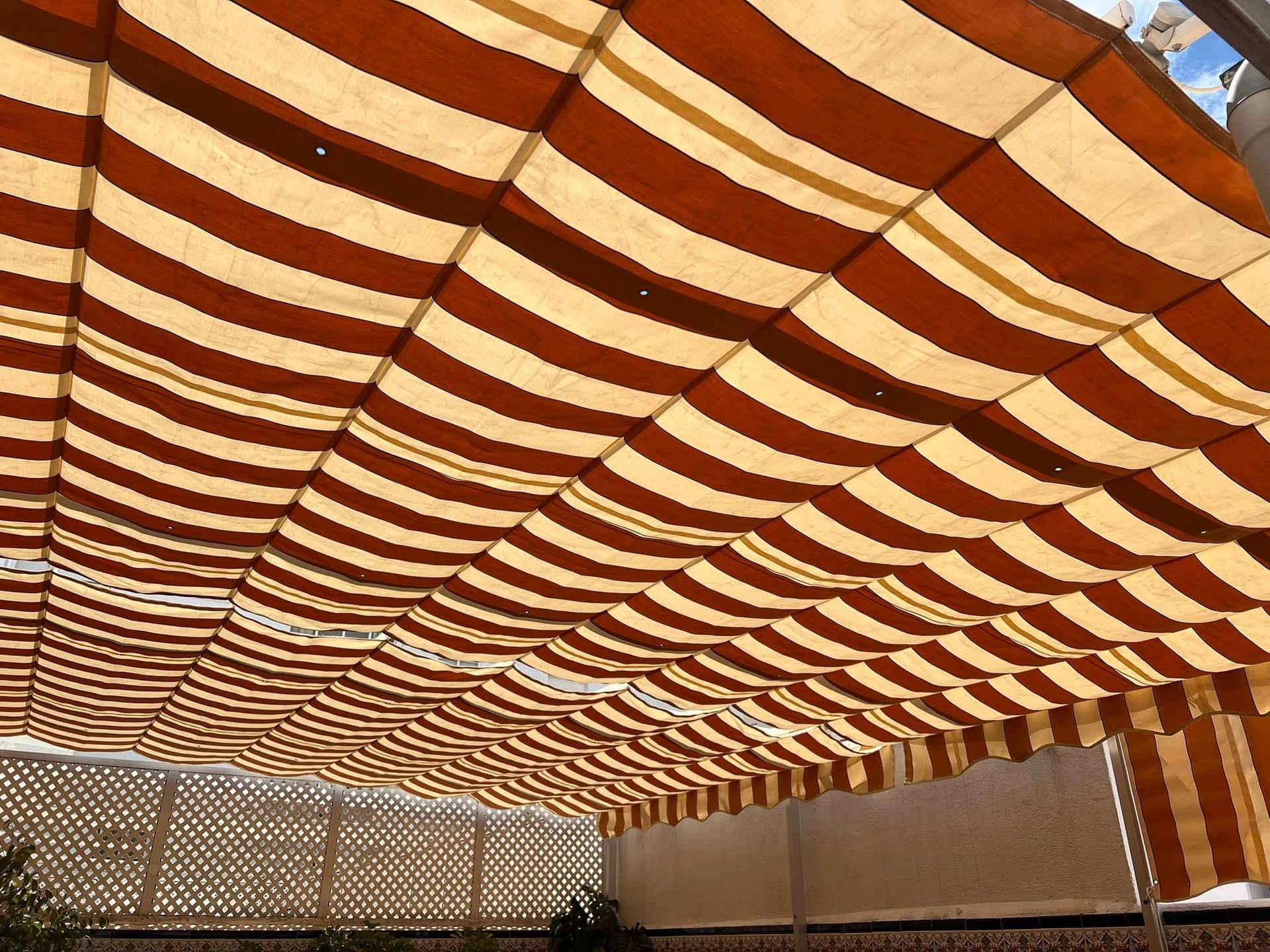 Toldo de rayas marrones y beige que proporciona sombra a un patio.