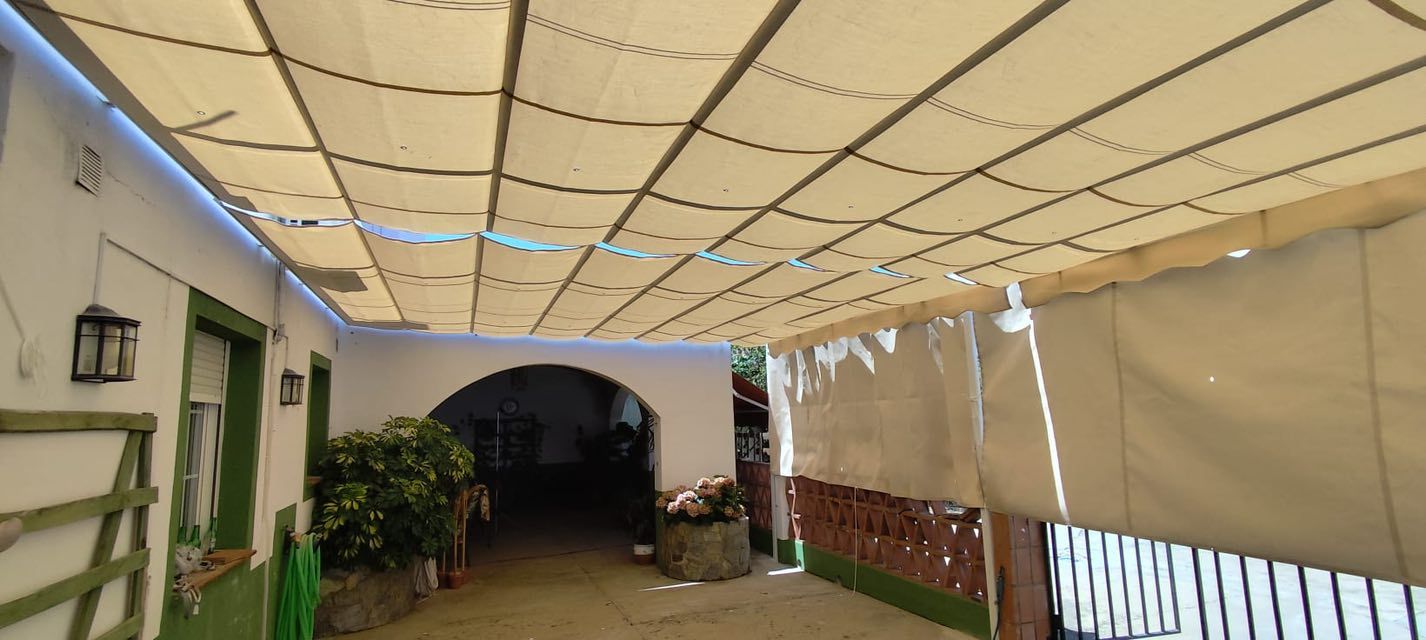 Pasarela exterior cubierta con paredes blancas, entrada arqueada y sombrillas beige.