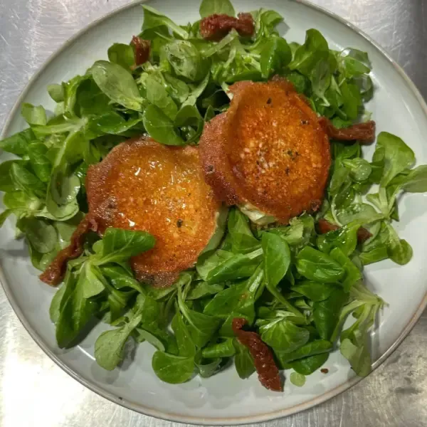 Ensalada con queso de cabra frito, tomates secos y lechuga verde en un plato blanco.