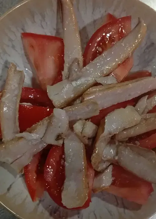 Ensalada de tomate y pescado blanco en un bol; tomates rojos y filetes de pescado de color marrón claro.