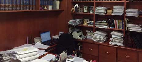 Una oficina desordenada con un escritorio, estantes de libros y papeles dispersos.