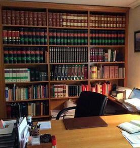 Estantería de madera llena de libros de derecho detrás de un escritorio con una silla negra en un entorno de oficina.