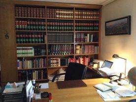 Oficina de madera con estanterías, escritorio, silla y computadora portátil; una lámpara encendida ilumina el escritorio.