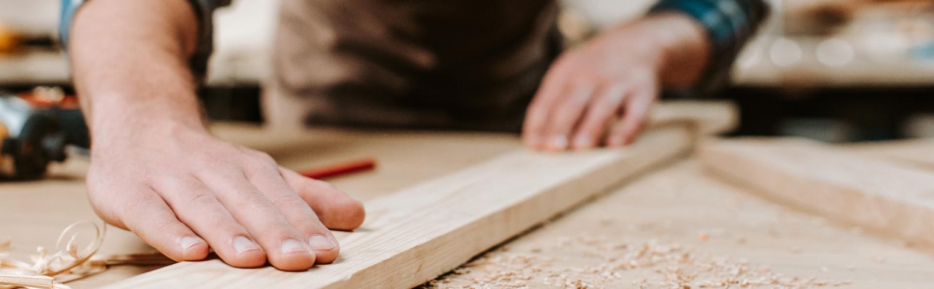 Die Hände einer Person an einem Stück Holz, vermutlich bei der Arbeit in einer Holzwerkstatt.