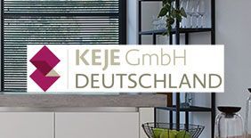 Logo der KEJE GmbH Deutschland über der Küchentheke. Dunkle Regale, im Hintergrund ein Fenster mit Jalousien.