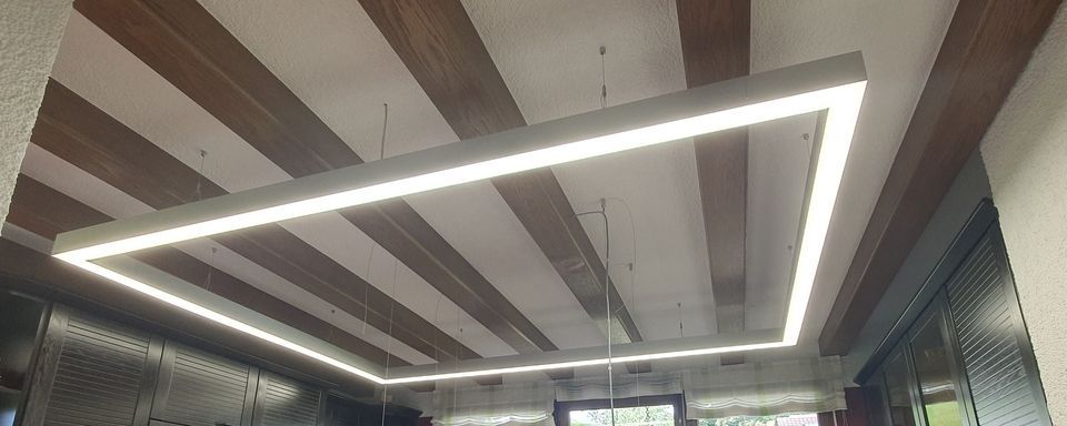 Eine rechteckige, beleuchtete Leuchte hängt von einer Decke mit abwechselnden Holz- und weißen Streifen herab.