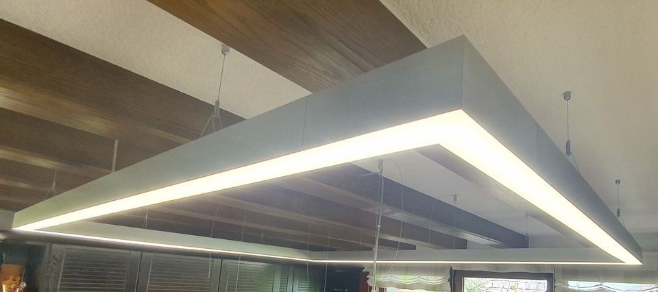 Rechteckige Leuchte, die von einer holzgetäfelten Decke herabhängt und über eine eingelassene Lampe verfügt, die ein helles Licht abgibt.