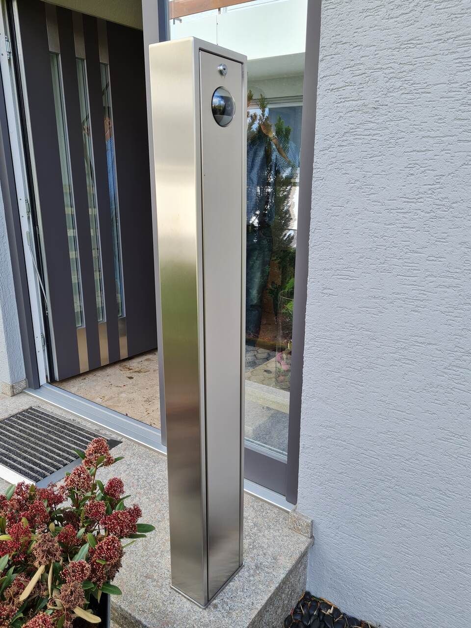 Briefkasten aus Edelstahl mit Kamera, montiert neben einer Tür auf einer Veranda.