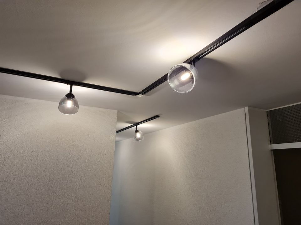 Ein schwarzes Schienensystem an einer weißen Decke beleuchtet weiße Wände und einen Türrahmen.