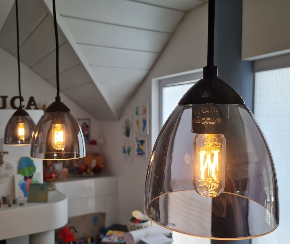 In einem Zimmer hängen drei Pendelleuchten mit klaren Glasschirmen und Edison-Glühbirnen.