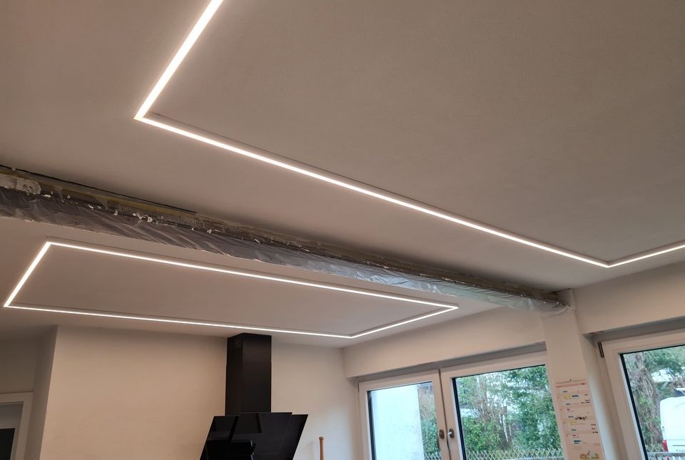 Weiße Decke mit eingelassenen rechteckigen LED-Leuchten; sichtbarer Balken mit freiliegender Verkabelung.