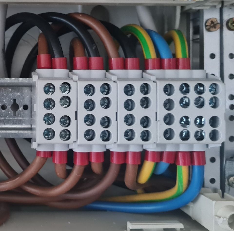 Elektrische Anschlussdose mit braunen, schwarzen, blauen, gelben und grünen Drähten, die an weiße Klemmen angeschlossen sind.