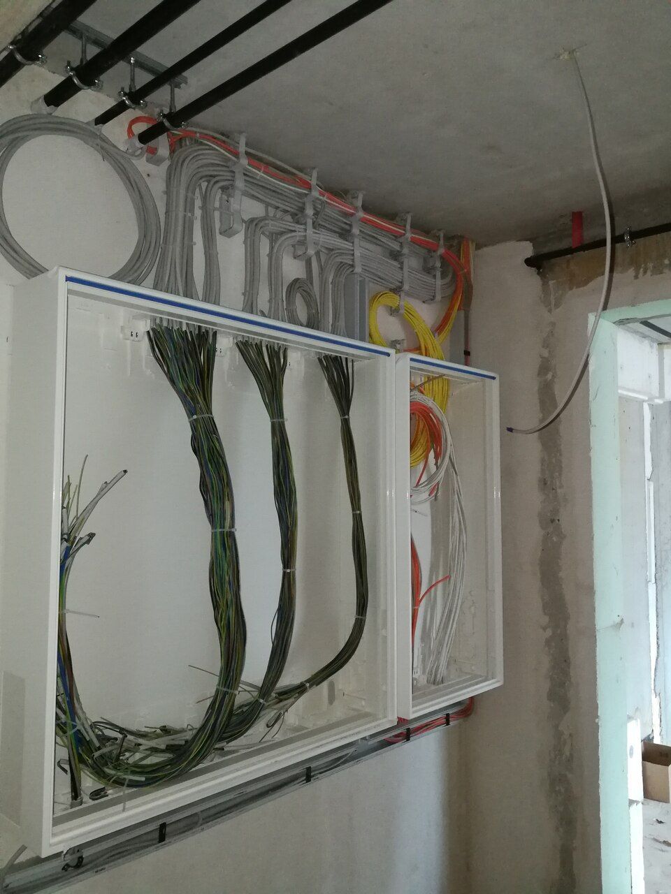 Elektroinstallation in einem Gebäude. Bündel farbiger Drähte in weißen Dosen an einer Wand, darüber verlaufen Leitungen.