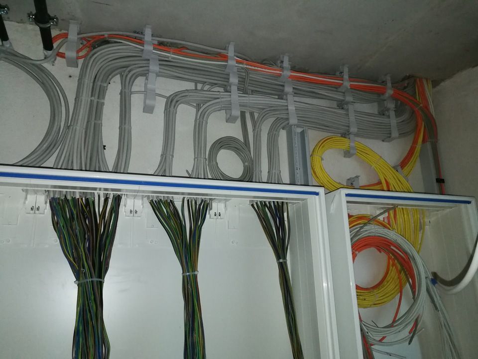 Elektrische Leitungen in verschiedenen Farben, geordnet an einer Wand in weißen Gehäusen.