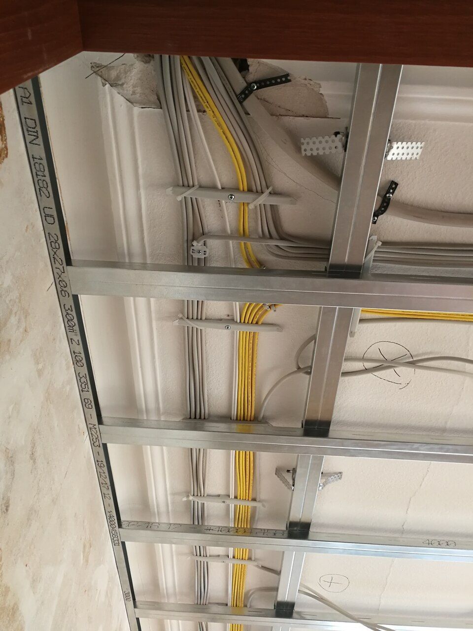 Die Decke befindet sich im Bau und weist freiliegende Leitungen, Metallrahmen sowie gelbe und graue Kabel auf.