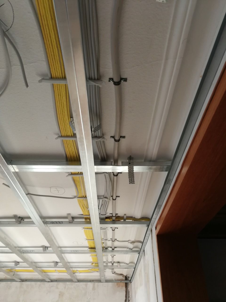 Draufsicht auf eine Decke mit einem Metallgittergerüst und mit schwarzen Klemmen befestigten elektrischen Leitungen.