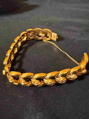 Pulsera de cadena dorada con eslabones gruesos tejidos sobre una superficie oscura.