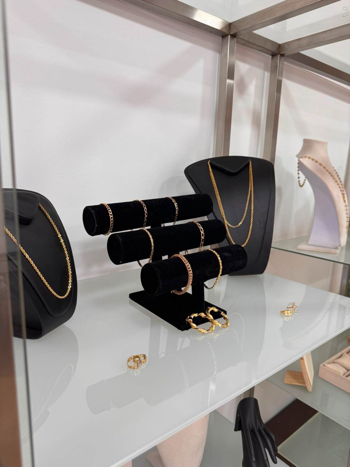 En el escaparate de una boutique, se exhiben joyas negras y doradas sobre soportes de terciopelo en una vitrina de cristal.