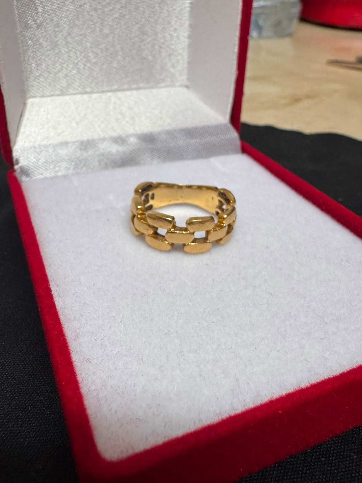 Anillo de cadena de oro en un joyero de terciopelo rojo sobre una superficie clara.